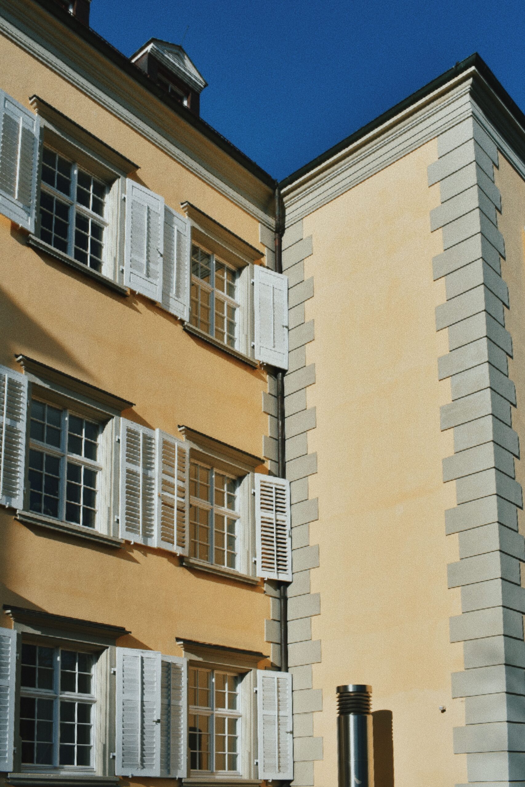 Historische Fassade in Ockergelb mit weißen Fensterläden, profilierten Fensterumrahmungen und grau abgesetzten Eckquadern
