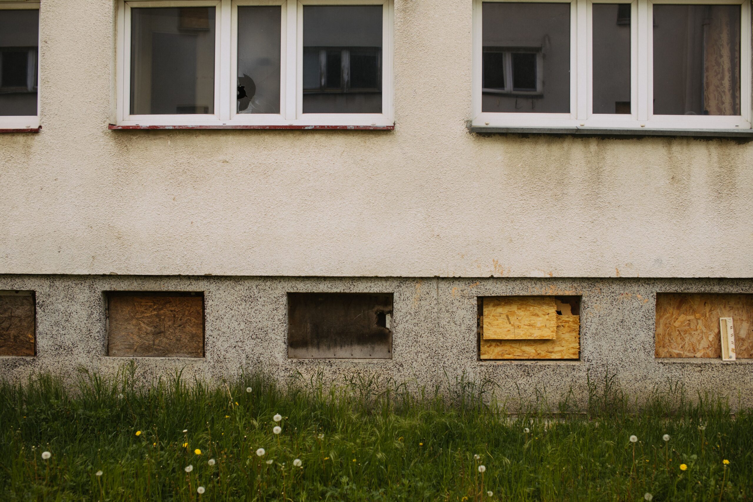 Verschmutzte Putzfassade mit dunklen Ablaufspuren unter den Fenstern und vergrautem Sockel