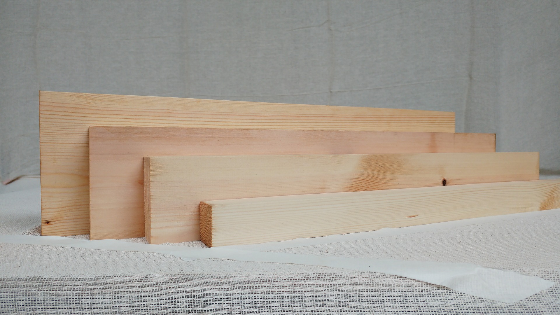Unbehandelte Sockelleisten aus hellem Holz in verschiedenen Höhen vor einer grauen Wand